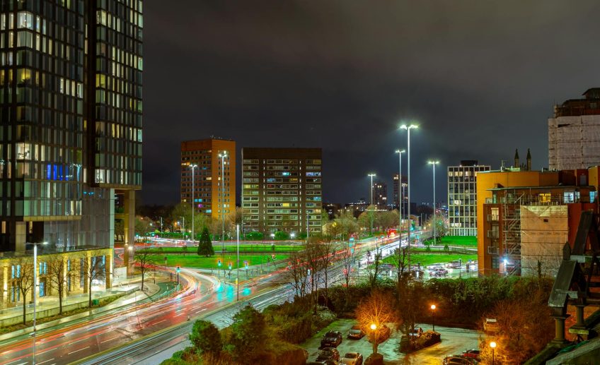 Cityscape of Manchester at night with buildings and illuminated streets, showcasing urban life