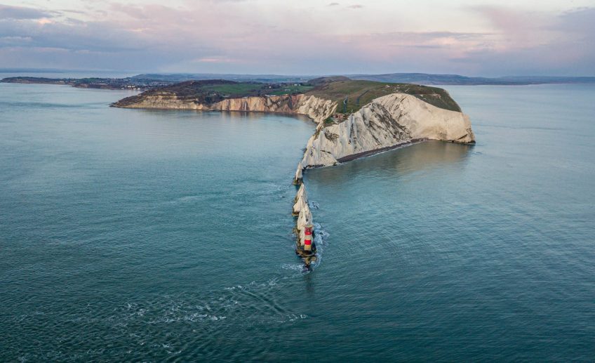 Stunning aerial view of a lighthouse on rugged cliffs extending into the sea under an overcast sky