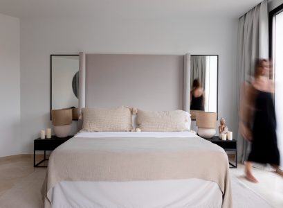 A woman walks by a bed, highlighting a serene and inviting bedroom atmosphere